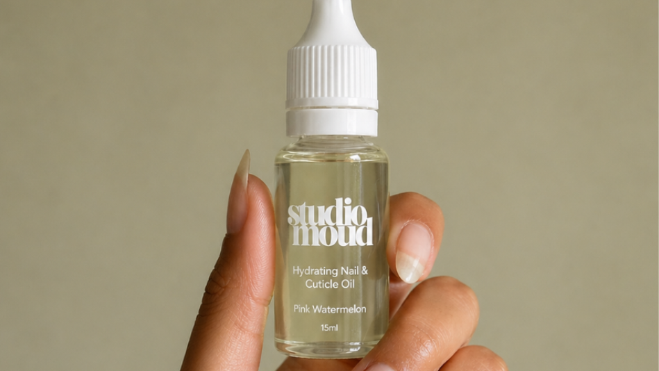 Hand holding a small bottle of Pink watermelon Cuticle Oil against a beige background